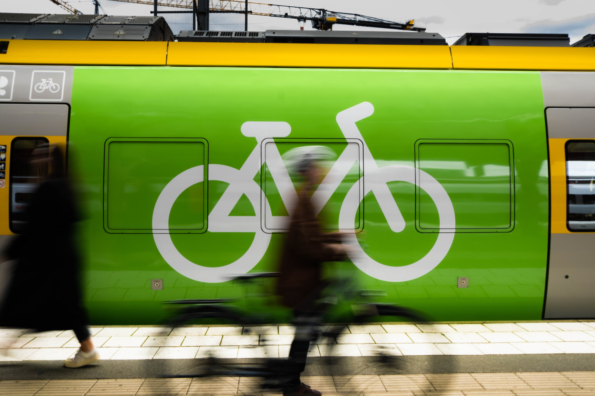 Visar grönt tåg med cykelsymbol, suddiga personer passerar.